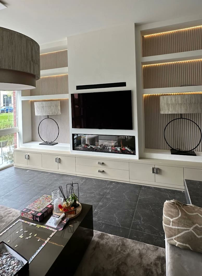 Cr&egrave;mekleurige cinewall met verlichte vakken, ribbelpanelen, televisie en driezijdige sfeerhaard