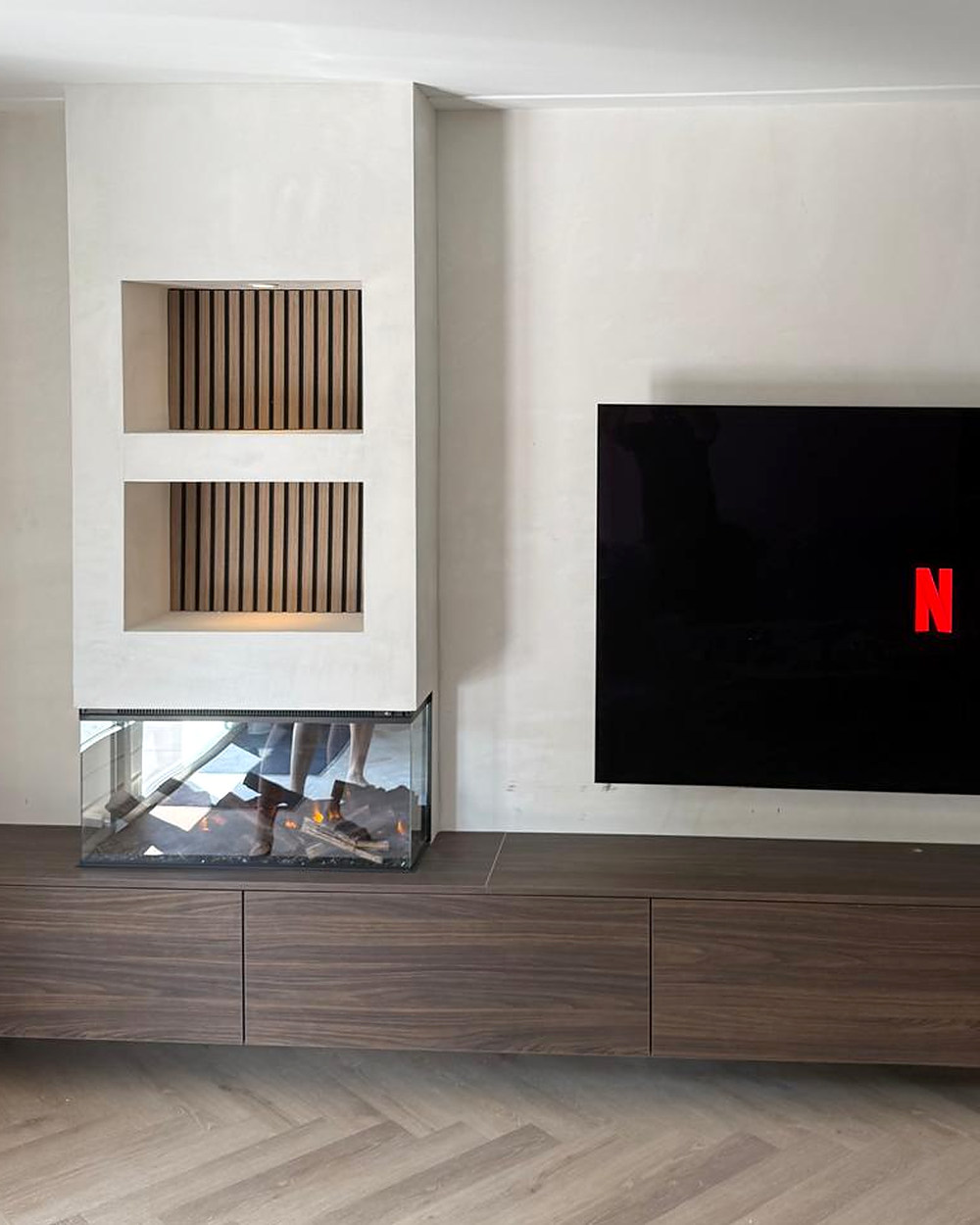 Het verhoogde deel met twee verlichte lattennissen boven de driezijdige haard, met het zwevende dressoir dat eronder doorloopt