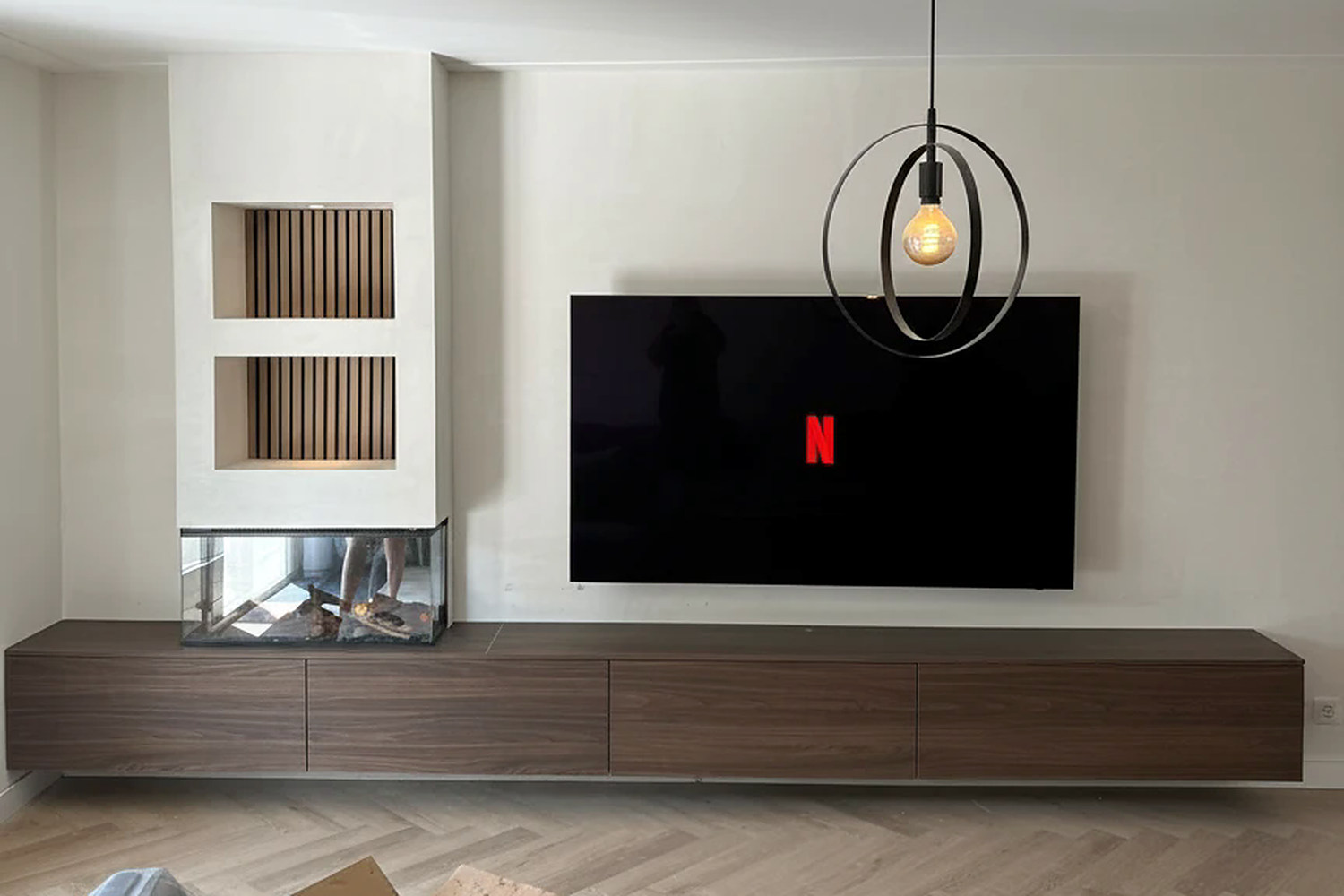 De hele cinewall met de hanglamp erboven: beide verlichte lattennissen, de driezijdige haard, de televisie en het zwevende dressoir over de volle breedte