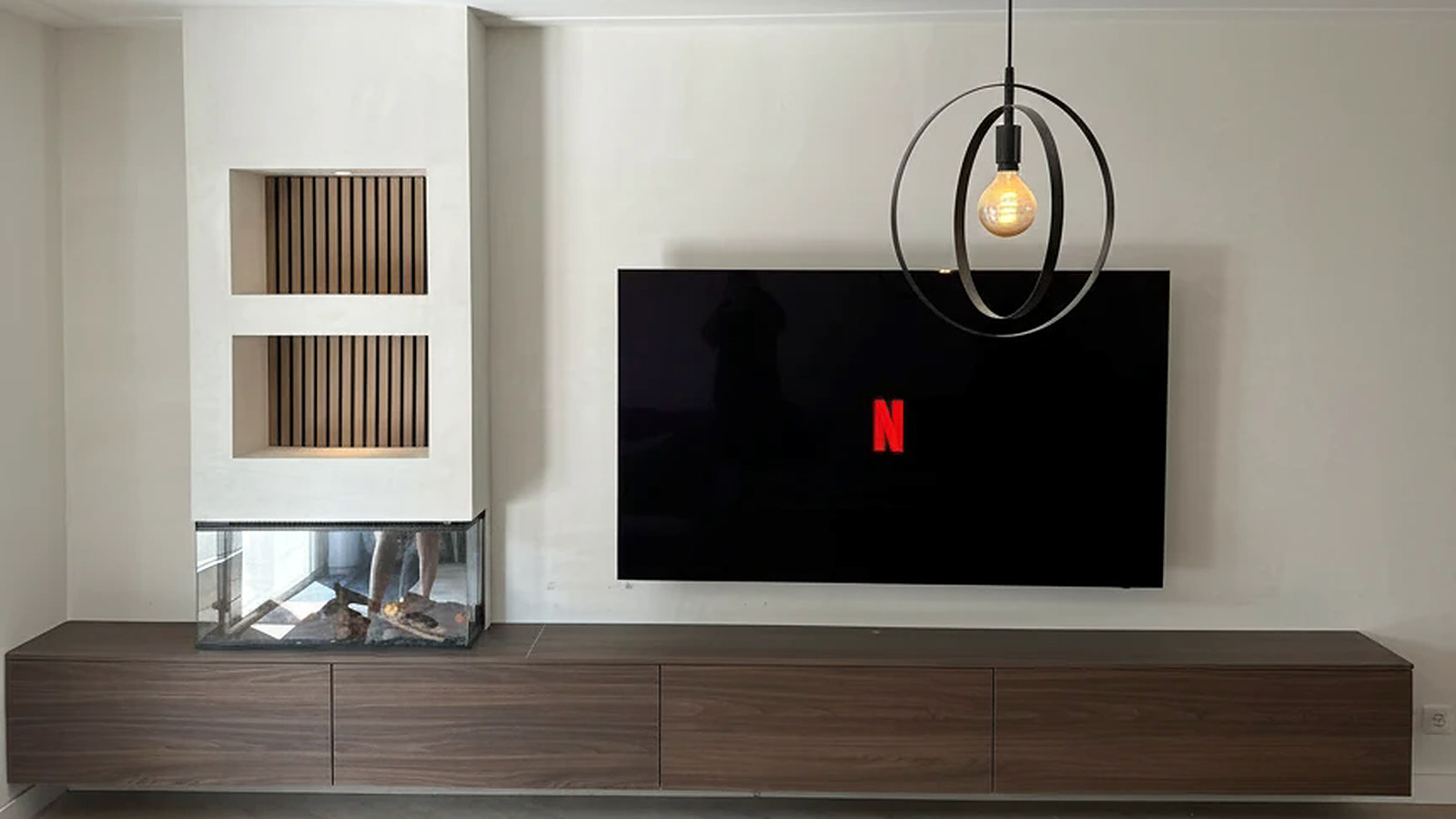 De volledige cinewall met de hanglamp erboven: beide verlichte lattennissen, de driezijdige haard, de televisie en het zwevende dressoir over de volle breedte