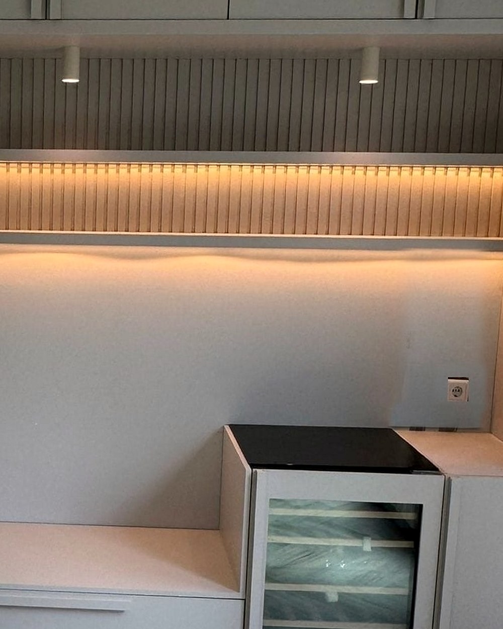 De rechterkant van de nis van dichtbij: het ribbelpaneel met de lichtlijn eronder, de opbouwspot en de wijnklimaatkast onder het zwarte werkblad