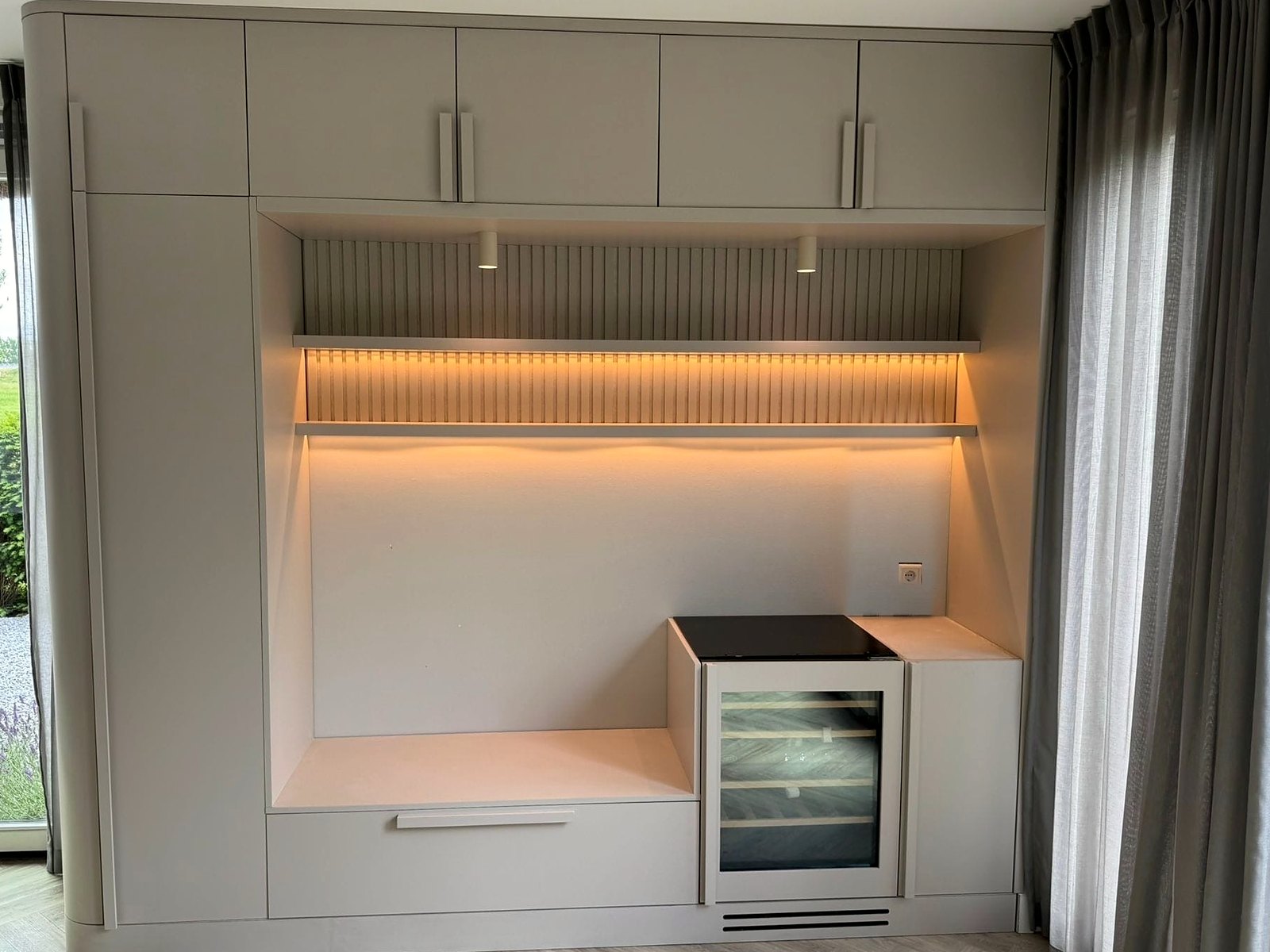 Maatwerk wandkast in greige met verlichte nis, ribbelpaneel, wijnklimaatkast en zitbank
