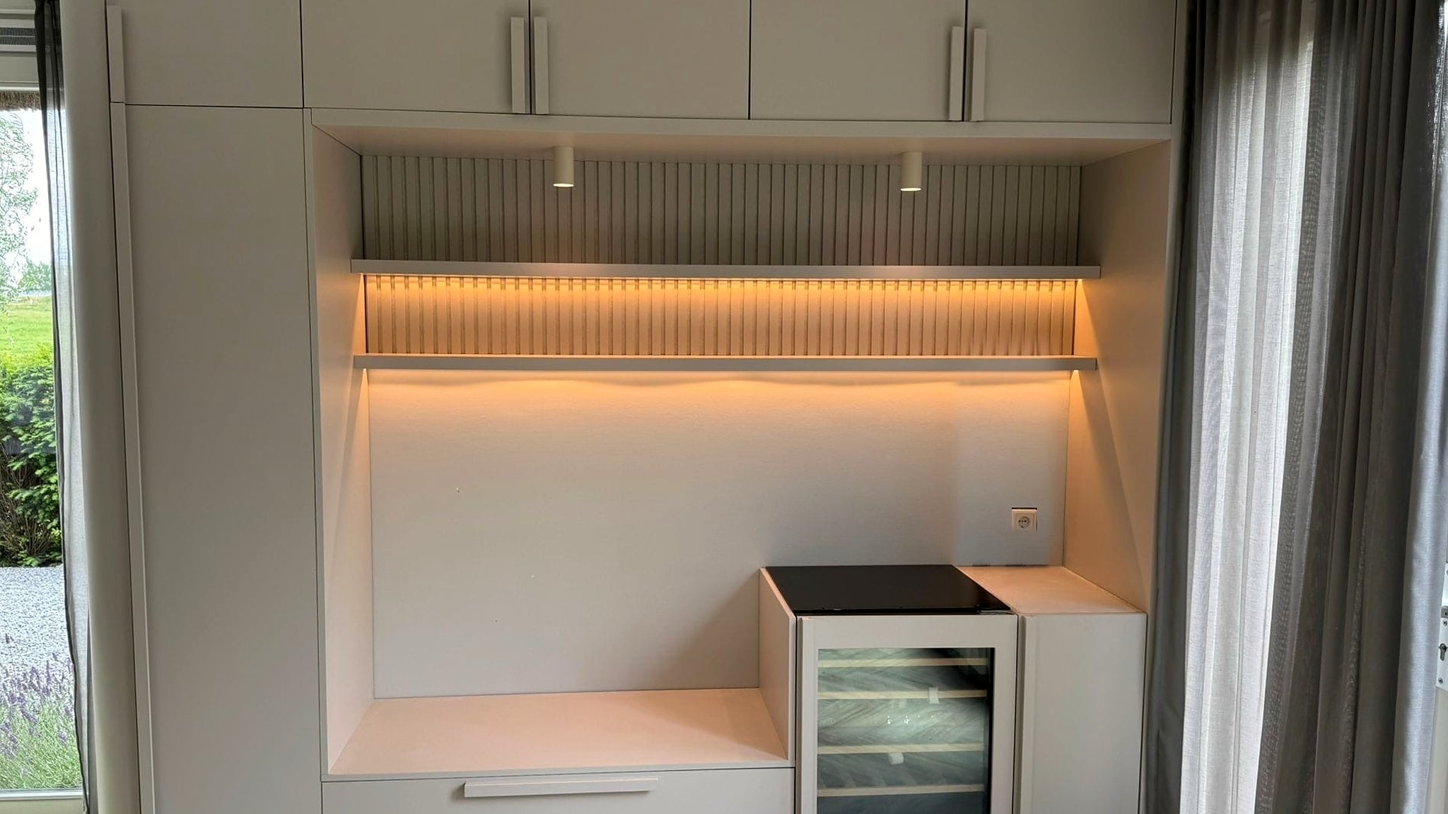 Maatwerk wandkast in greige met een verlichte nis, ribbelpaneel, wijnklimaatkast en zitbank